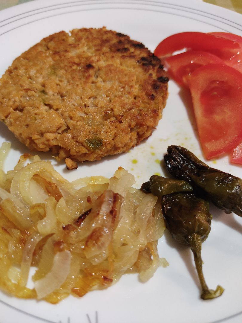 Hamburguesa de soja texturizada con acompañamiento de cebolla y pimientos fritos y tomate natural