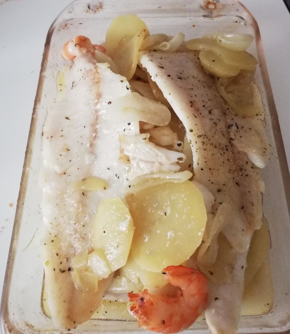 Merluza al horno con langostinos, patatas y cebolla.