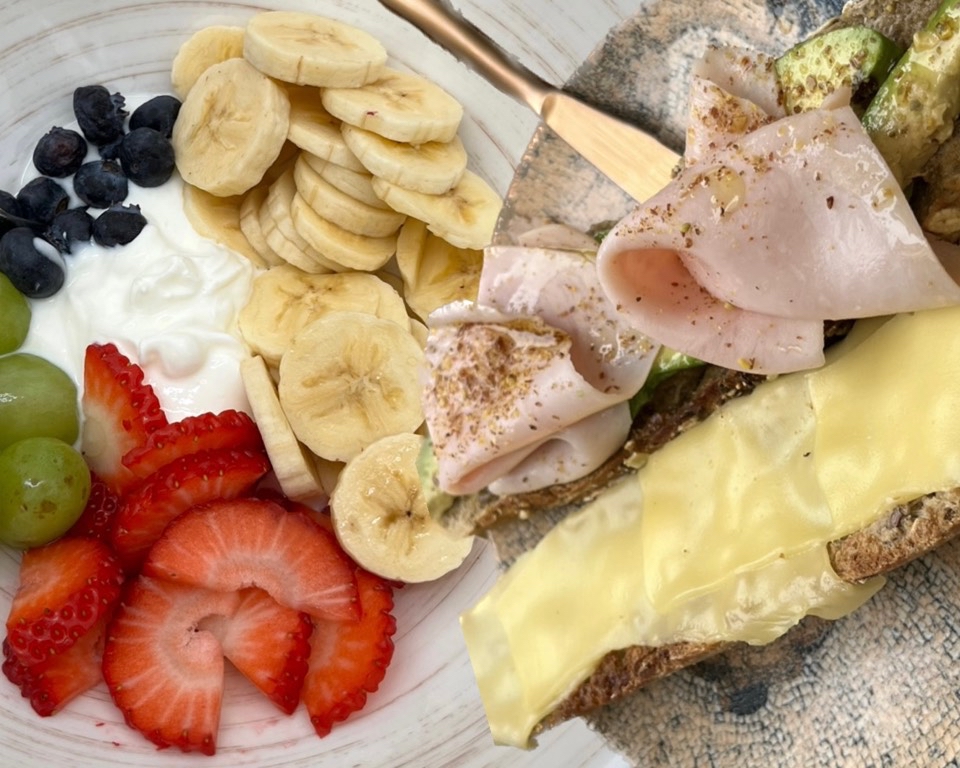 Yogur natural con uvas, moras, plátano y fresas + tostada de pan integral de semillas con queso, aguacate y pavo.
