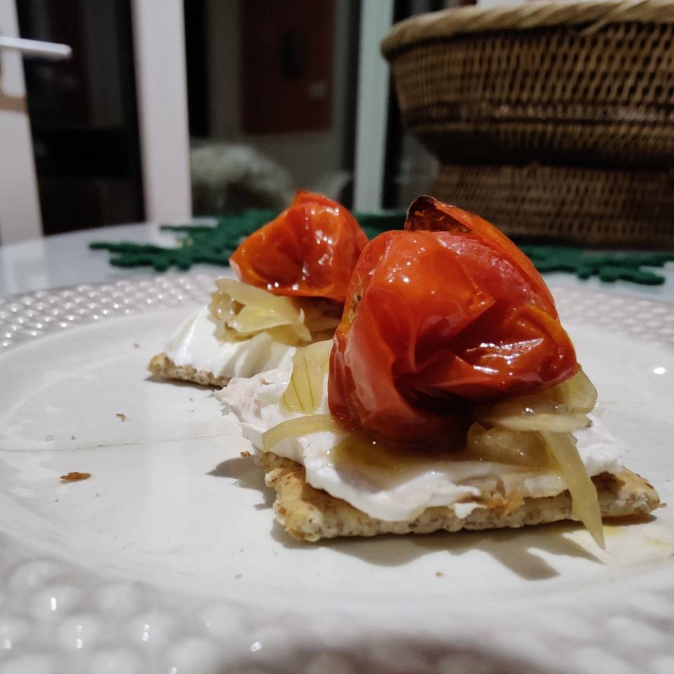 Tosta integral con queso crema, cebolla caramelizada y tomate cherry asaso.