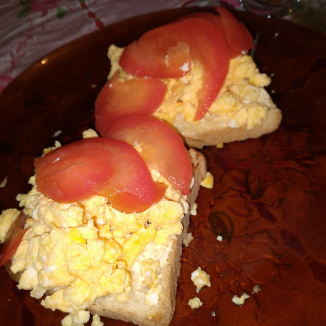 Tostada con huevos revueltos y tomate en rodajas.